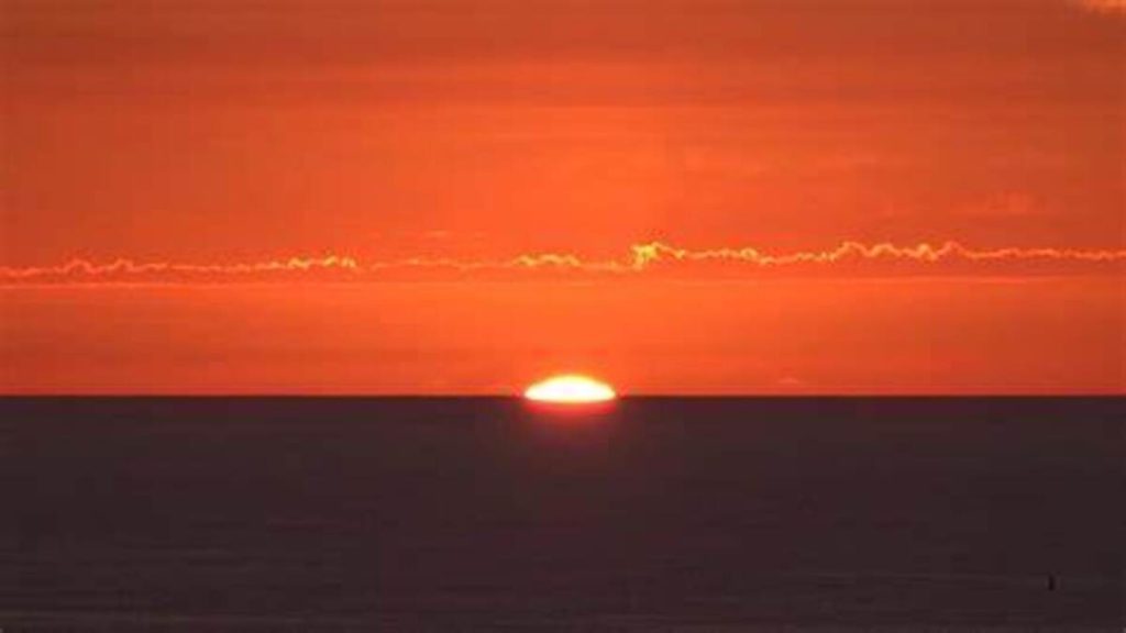 Fotografía de una impresionante puesta de sol en una hermosa costa, donde el cielo se tiñe de tonalidades doradas y rojizas.