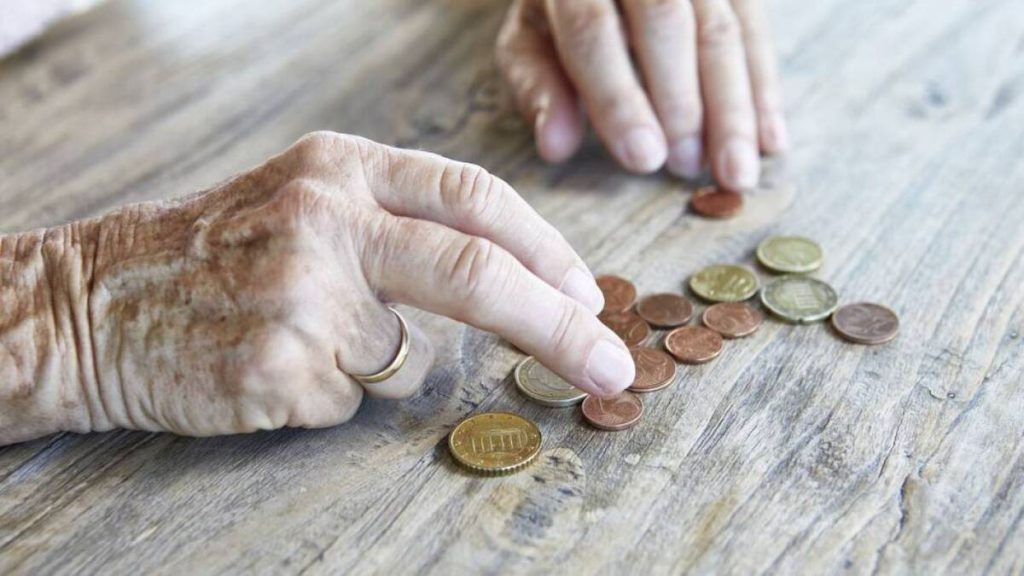 Mano arrugada de un adulto mayor contando monedas para administrar sus recursos económicos.